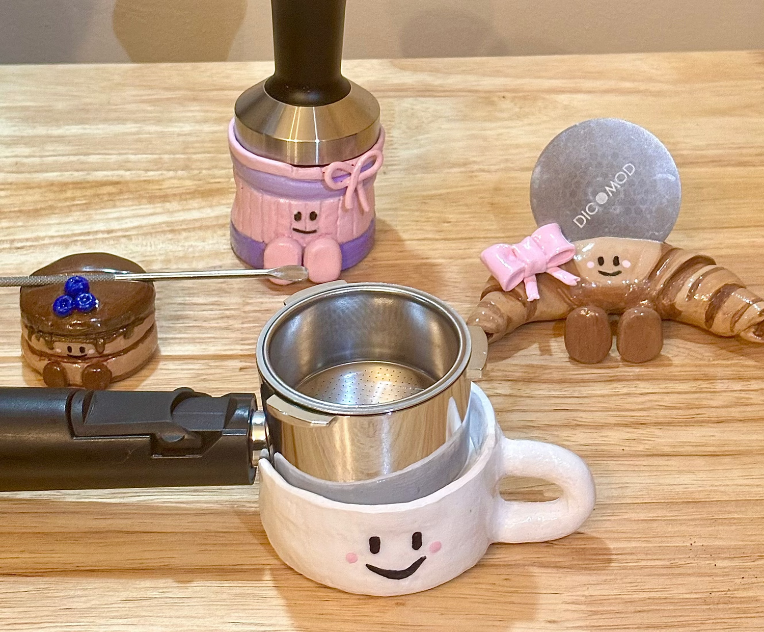 Coffee-making tools including a portafilter, tamper, and decorative items on a wooden surface.